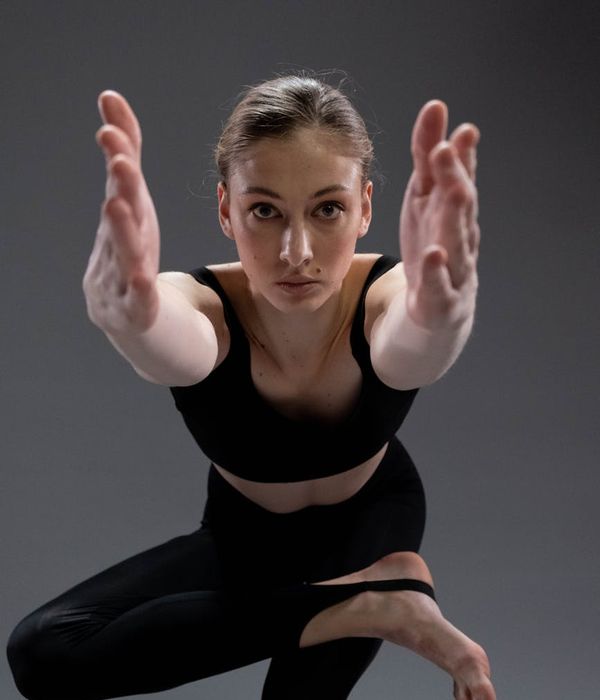 Woman in a calming yoga pose against a dark grey background.